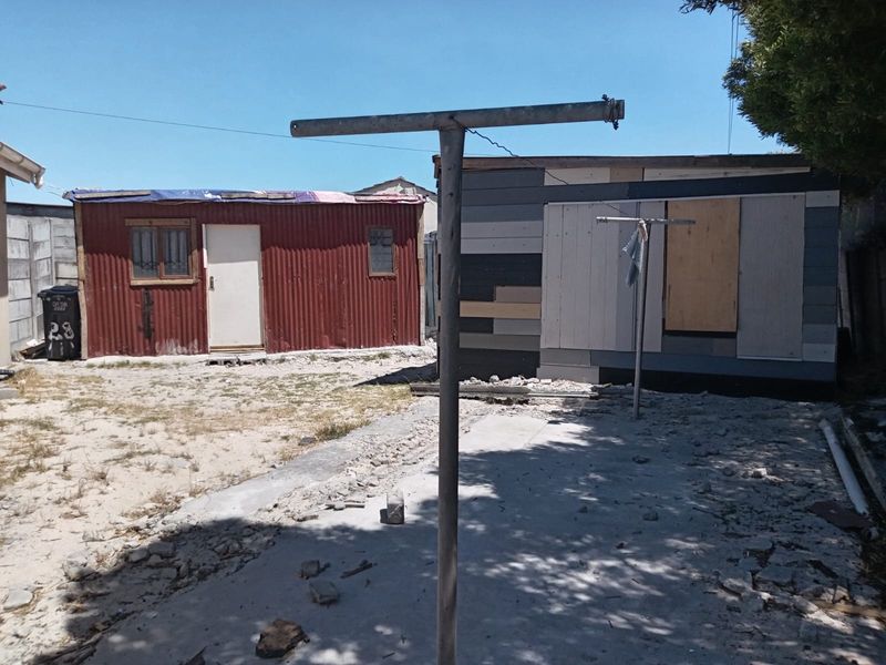 Rear yard area featuring a corrugated metal structure and a concrete slab, showing significant signs of wear and maintenance requirements.
