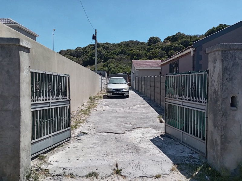 A view of the property entrance featuring a concrete driveway, perimeter walling, and metal security gates.