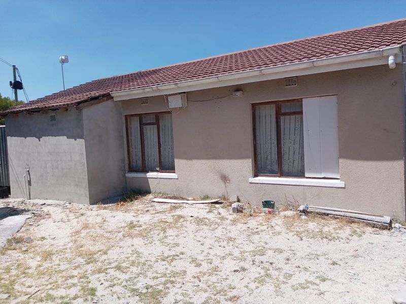 Rear exterior view of the house showing tiled roofing, aluminium window frames, and unfinished plasterwork on the side wall.