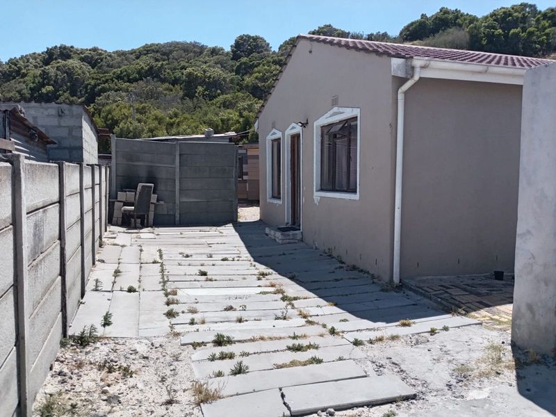 Rear exterior view of the property featuring a paved walkway, concrete boundary walls, and a tiled roof structure.