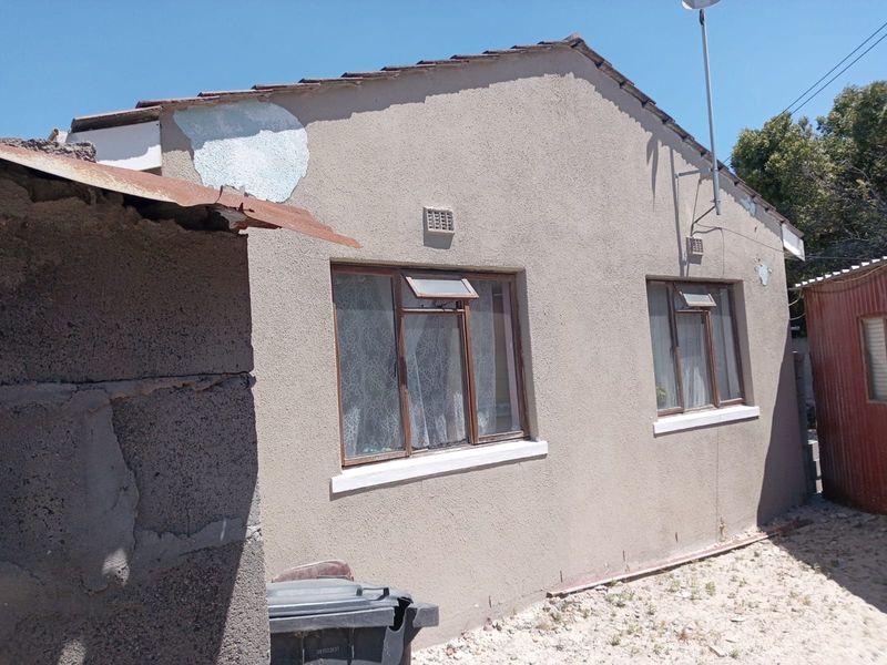 Rear exterior view of the house showing a tiled roof, brown aluminium window frames, and visible signs of exterior wall plaster and paint deterioration.