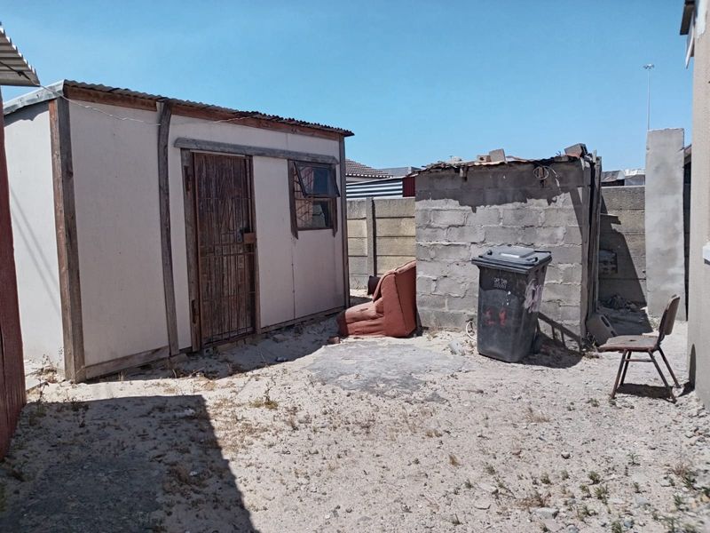 Rear yard area featuring a prefabricated shed, concrete block boundary wall, and basic outdoor space with sandy ground.