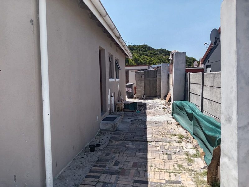 A narrow rear exterior side passage featuring paved flooring and a precast concrete boundary wall, showing signs of wear and unfinished exterior surfaces.