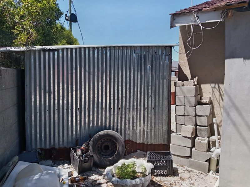Rear exterior area featuring corrugated metal fencing and exposed masonry, requiring maintenance and cleanup of the surrounding space.