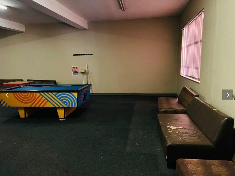 A spacious clubhouse or recreational room featuring exposed ceiling beams, vertical blinds, and basic lighting, currently used as a games area.