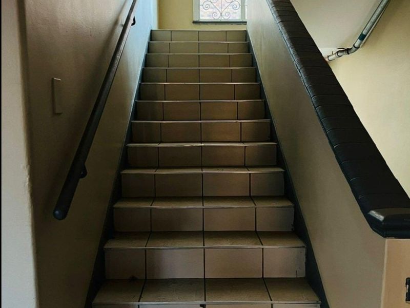 A functional interior stairwell featuring tiled steps, a handrail, and a window with a decorative security grille.