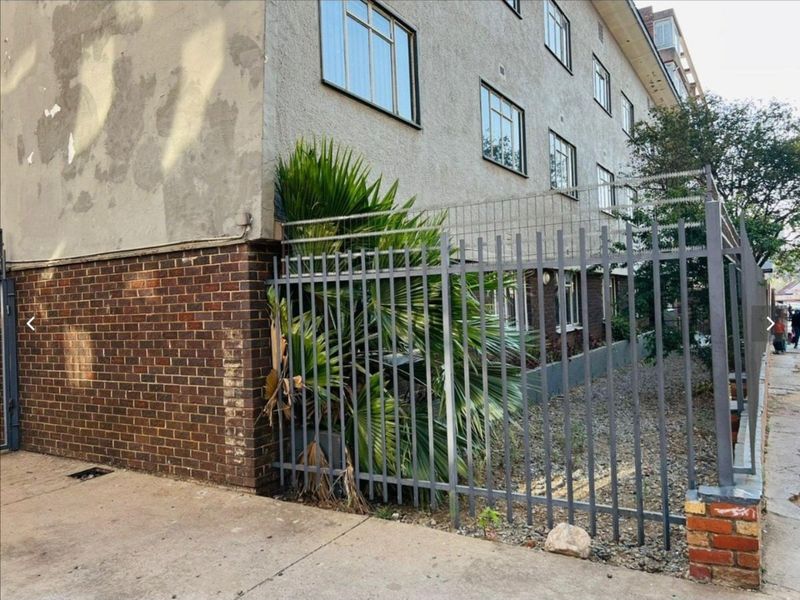 Exterior view of an apartment building featuring a brick and plastered facade with metal security fencing and casement windows.