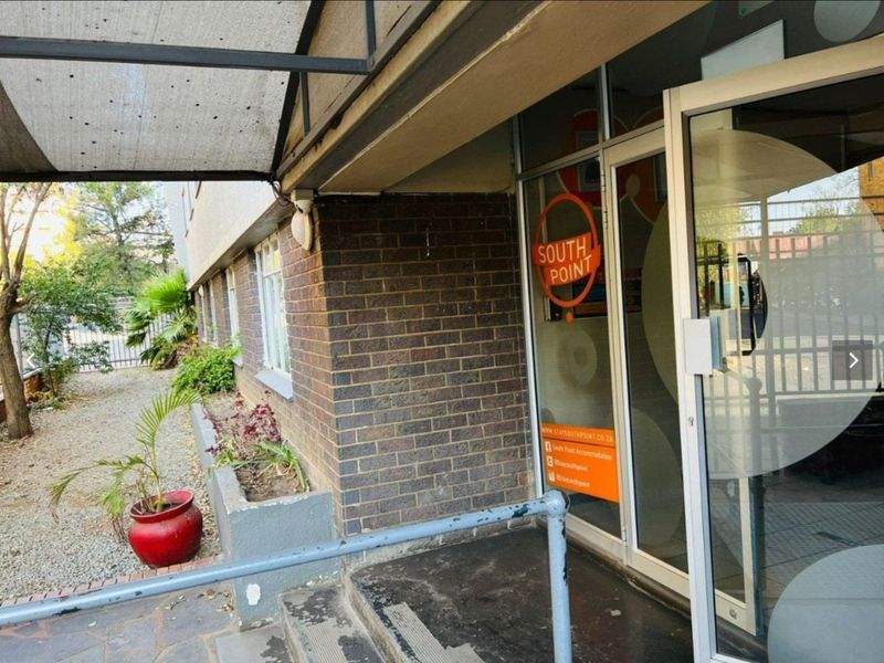 Exterior entrance area featuring a brick facade, glass door, and concrete steps with a metal handrail.
