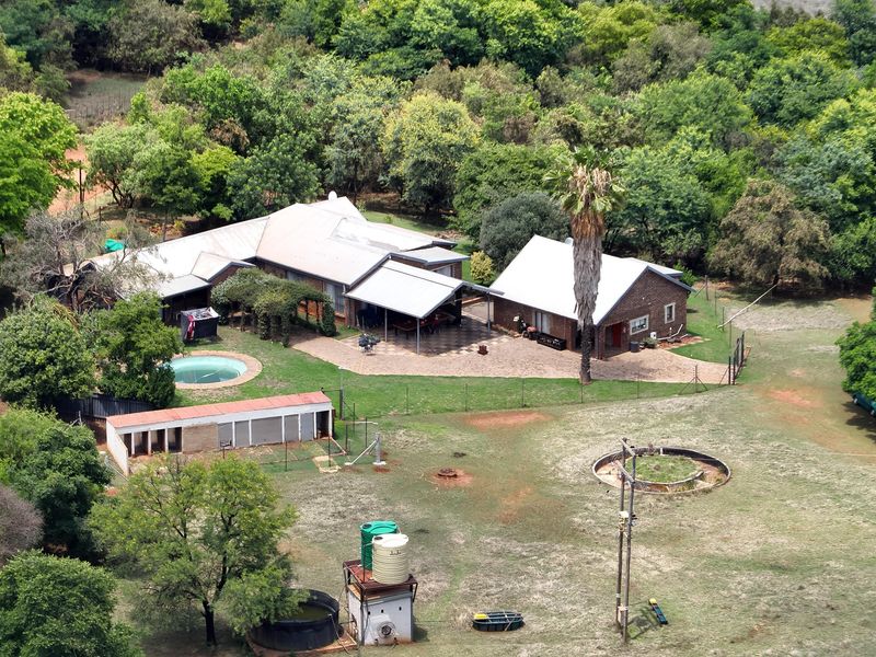 Aerial view of a farm property featuring a main residence with a swimming pool, paved patio, outbuildings, and water storage infrastructure set in landscaped grounds.