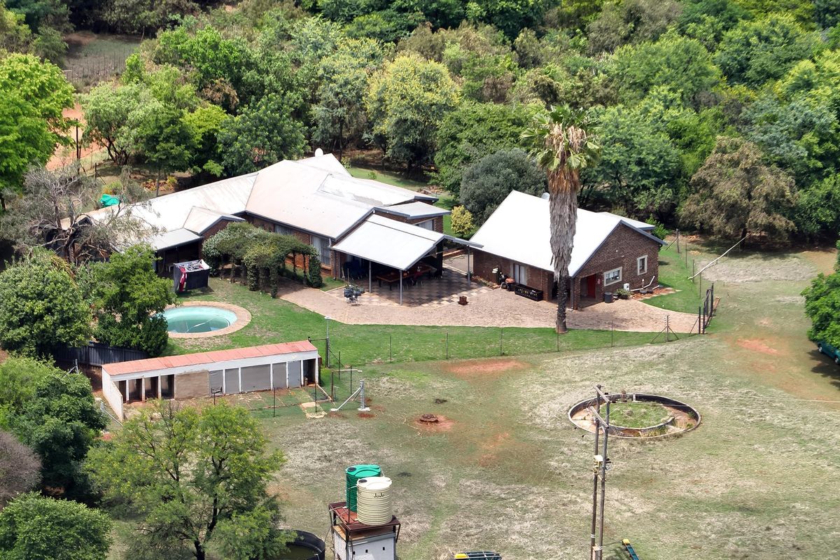 Aerial view of a farm property featuring a main residence with a swimming pool, paved patio, outbuildings, and water storage infrastructure set in landscaped grounds.
