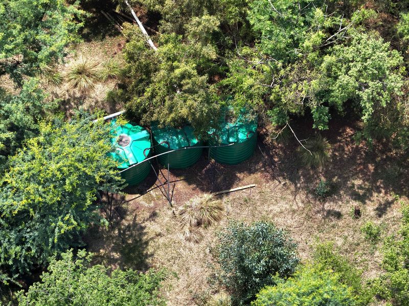 Aerial view of three green water storage tanks situated within a wooded area on the farm property.