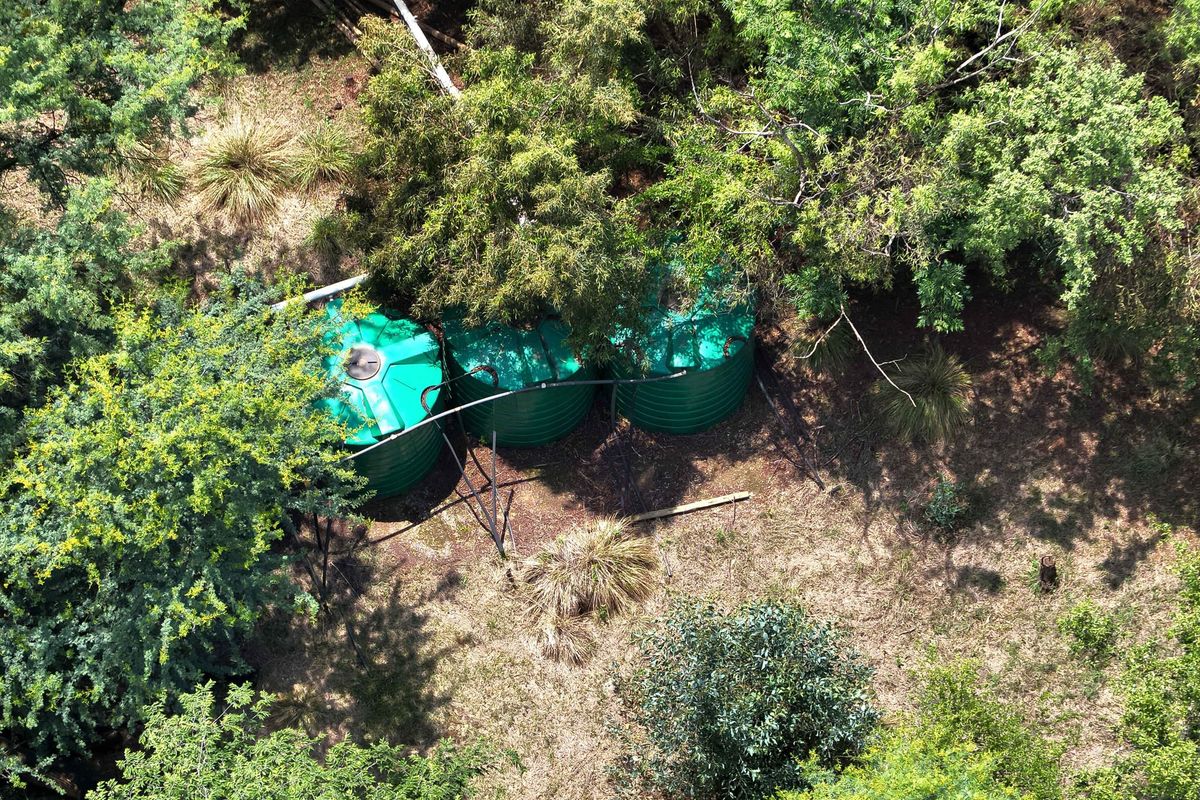 Aerial view of three green water storage tanks situated within a wooded area on the farm property.