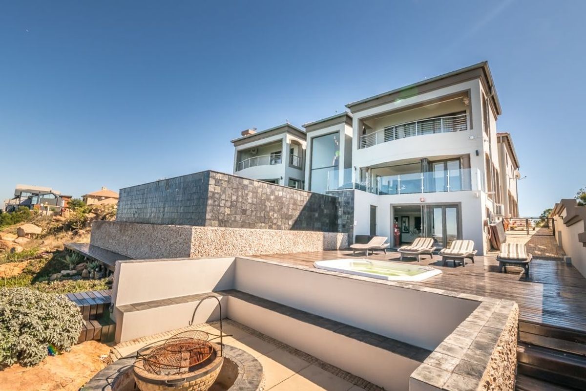 Spacious rear exterior featuring multi-level timber decking, a built-in fire pit, and a spa area with modern glass balustrades and stone cladding.