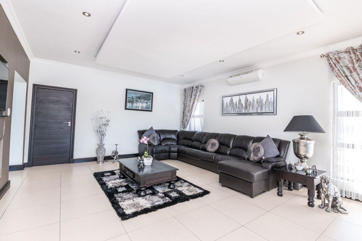 A bright and spacious living room featuring tiled flooring, a recessed ceiling with downlights, and a wall-mounted air conditioning unit.