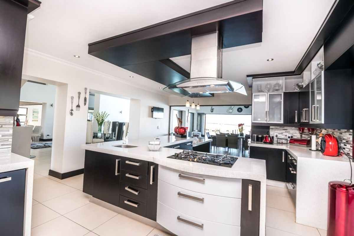 Modern kitchen featuring dark and white cabinetry, stone countertops, a central island with a gas hob, and an integrated extractor fan.