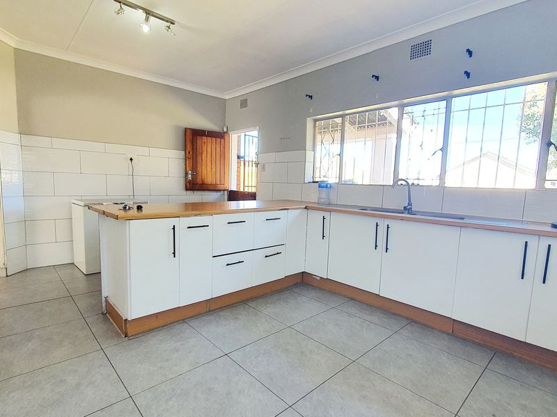 A functional kitchen featuring white cabinetry, wooden countertops, tiled backsplash, and large windows with security bars, offering a clean and bright workspace.