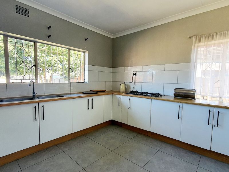 A functional kitchen featuring white cabinetry, laminate countertops, a gas hob, and tiled splashbacks, offering a clean and practical workspace.