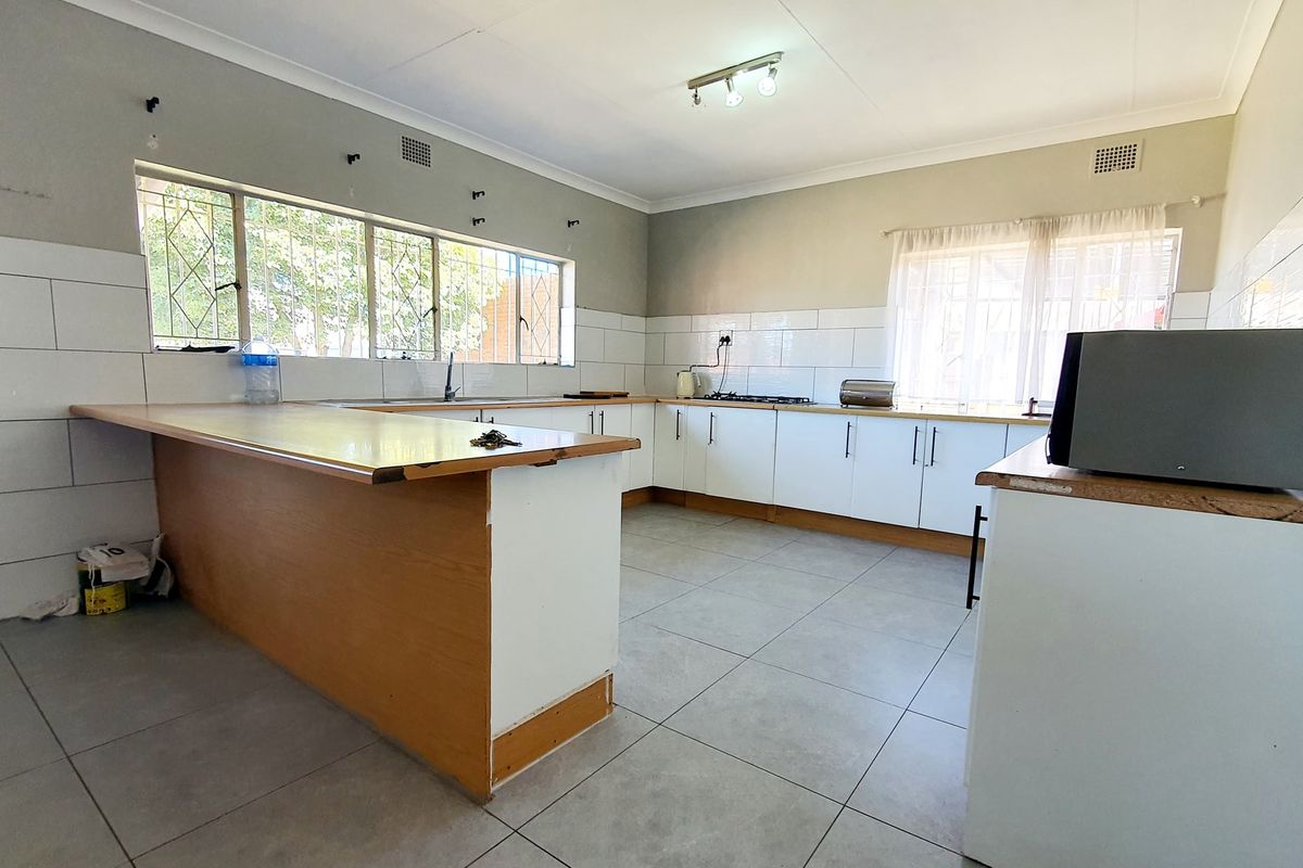 Spacious kitchen featuring white cabinetry, tiled splashbacks, and a large breakfast bar, offering a functional layout ready for modern updates.