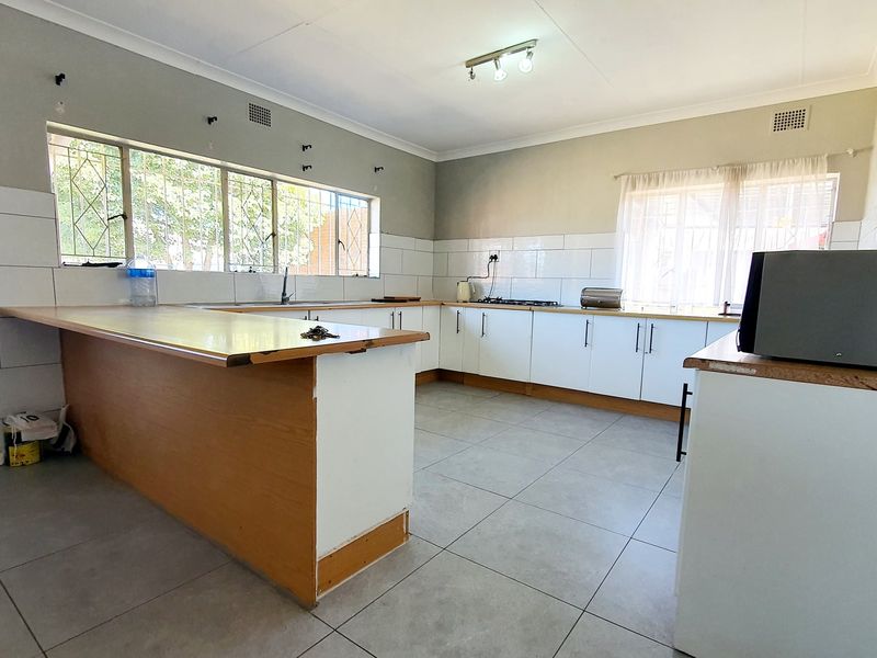 Spacious kitchen featuring white cabinetry, tiled splashbacks, and a large breakfast bar, offering a functional layout ready for modern updates.