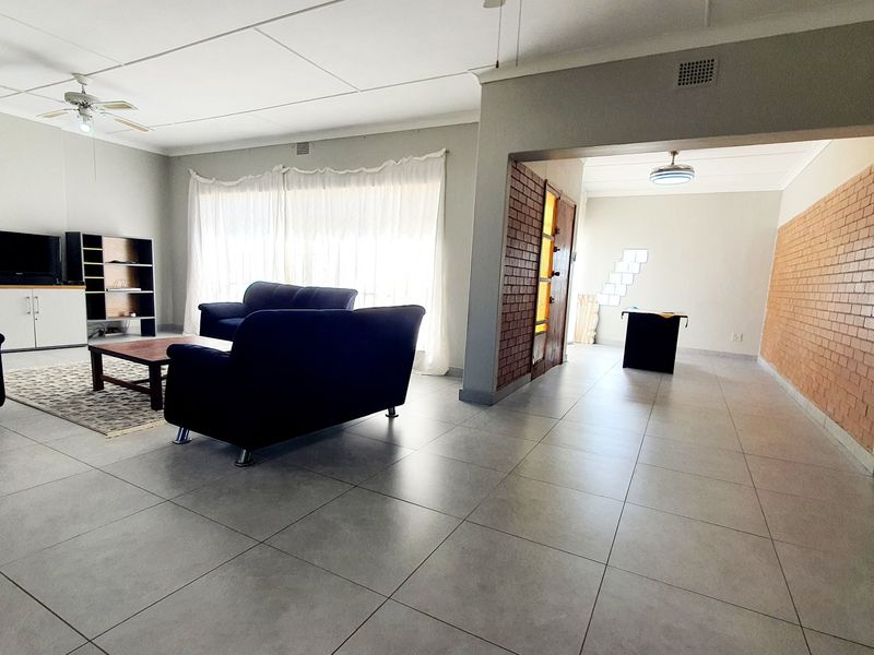 Spacious open-plan living area featuring large format floor tiles, an exposed brick feature wall, and a ceiling fan, offering a versatile layout.