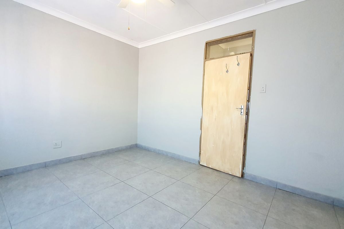 A vacant bedroom featuring neutral grey walls, tiled flooring, a ceiling fan, and a wooden internal door with a transom window.
