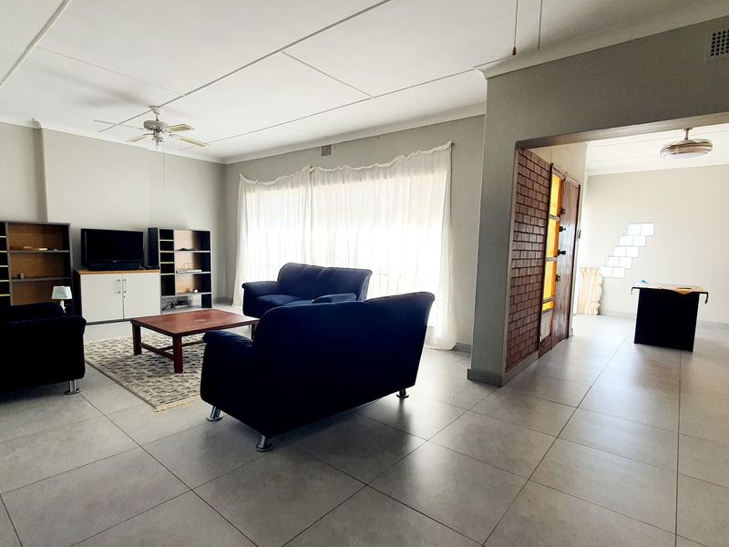 Spacious open-plan living area featuring neutral tiled flooring, a ceiling fan, and an exposed brick feature wall with natural light.