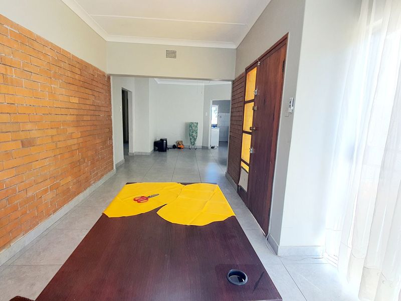 Spacious living area featuring an exposed brick feature wall, neutral tiled flooring, and direct access to adjacent rooms.