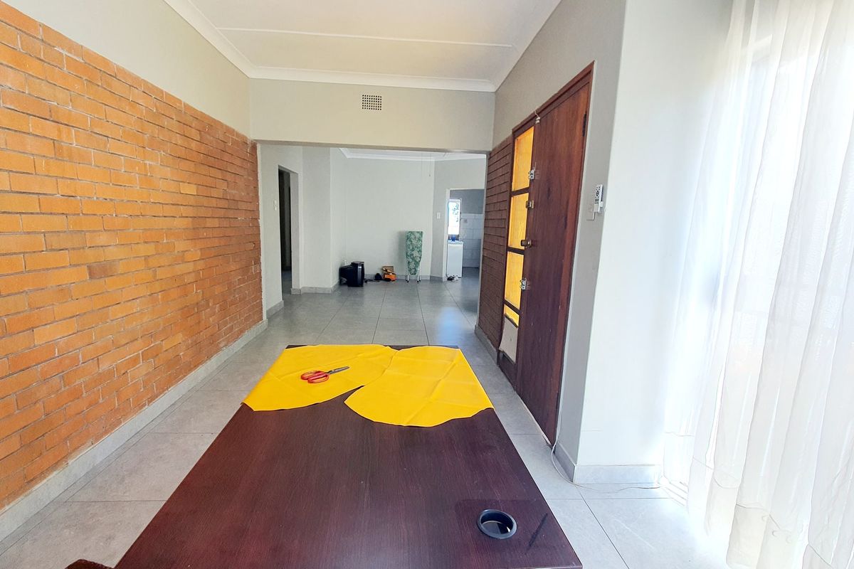 Spacious living area featuring an exposed brick feature wall, neutral tiled flooring, and direct access to adjacent rooms.