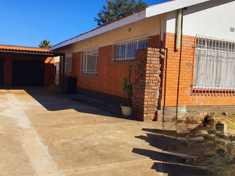 Front exterior view of a brick house featuring a concrete driveway, carport, and security bars on windows.