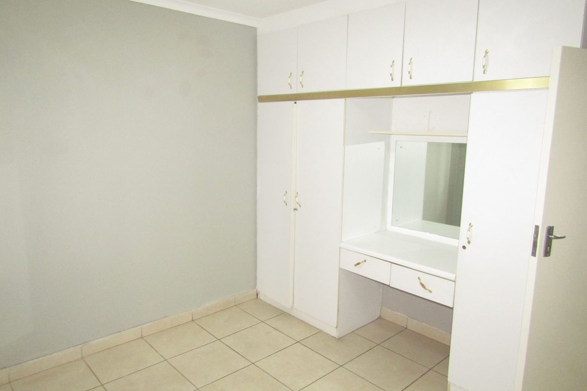 A clean, empty bedroom featuring neutral wall paint, tiled flooring, and extensive built-in white cabinetry with an integrated vanity area.