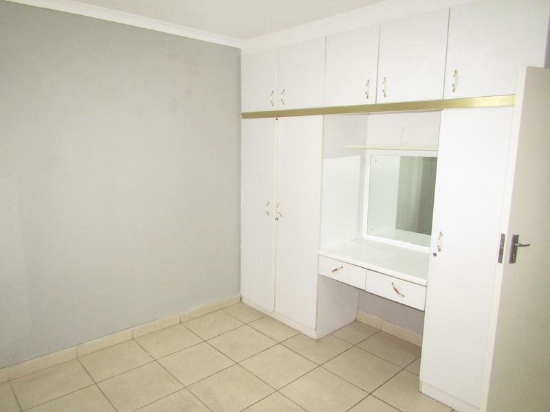 A clean, empty bedroom featuring neutral wall paint, tiled flooring, and extensive built-in white cabinetry with an integrated vanity area.