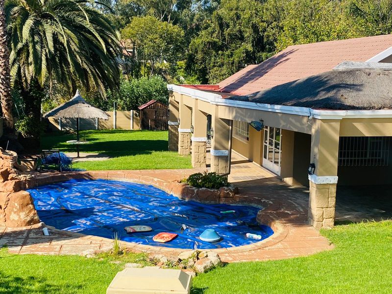 Outdoor entertainment area featuring a swimming pool with a cover, adjacent to a covered patio with stone-clad pillars and a landscaped garden.