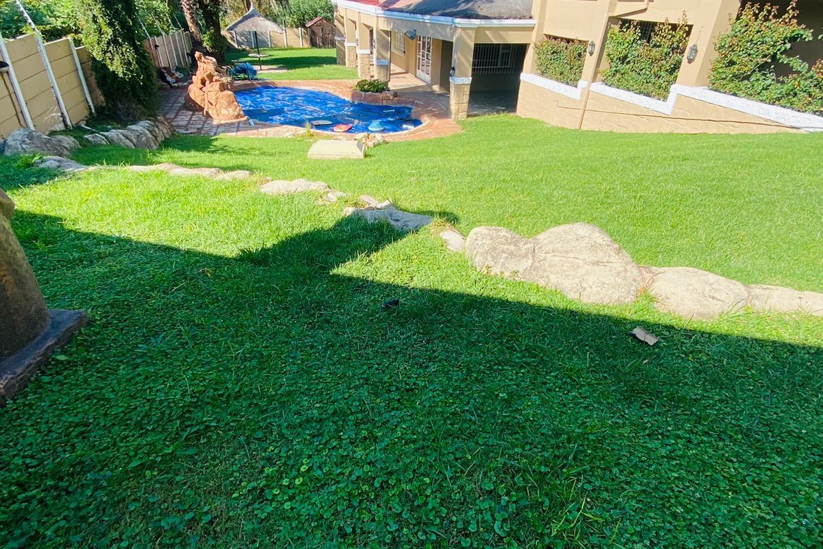 Spacious rear garden featuring a swimming pool, well-maintained lawn, and a covered patio area attached to the main house structure.