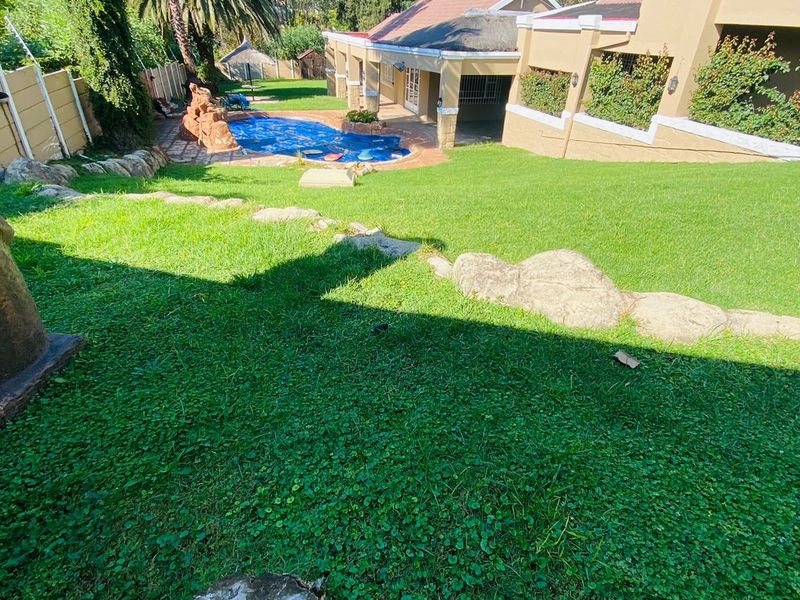 Spacious rear garden featuring a swimming pool, well-maintained lawn, and a covered patio area attached to the main house structure.