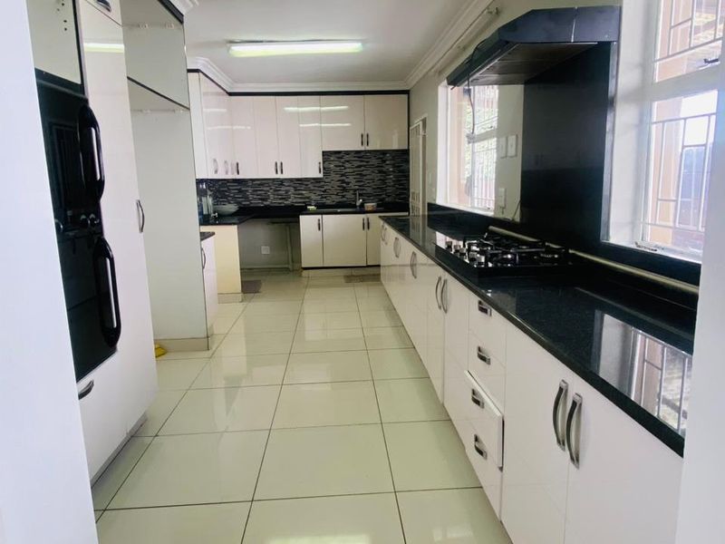 A clean, galley-style kitchen featuring white cabinetry, black granite countertops, built-in oven, gas hob, and tiled flooring.