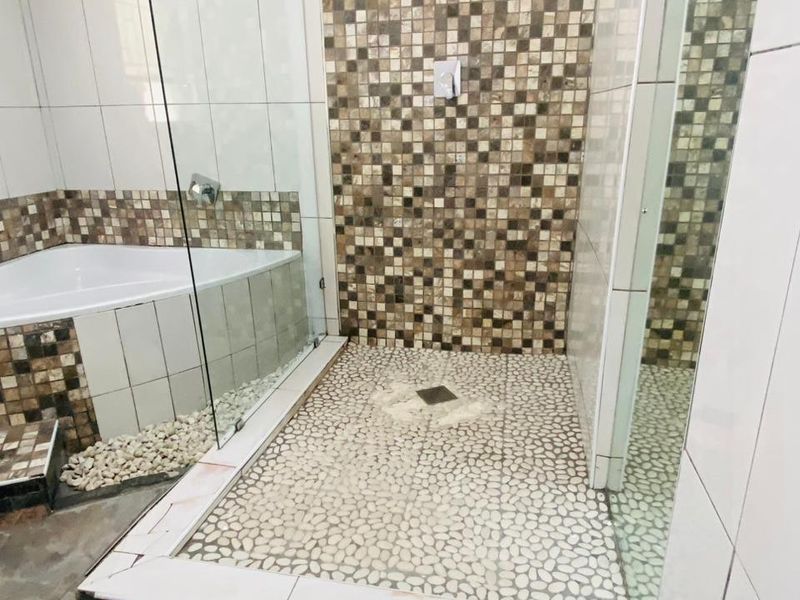A bathroom featuring a walk-in shower with pebble flooring and mosaic wall tiles, alongside a built-in bathtub with glass enclosure.