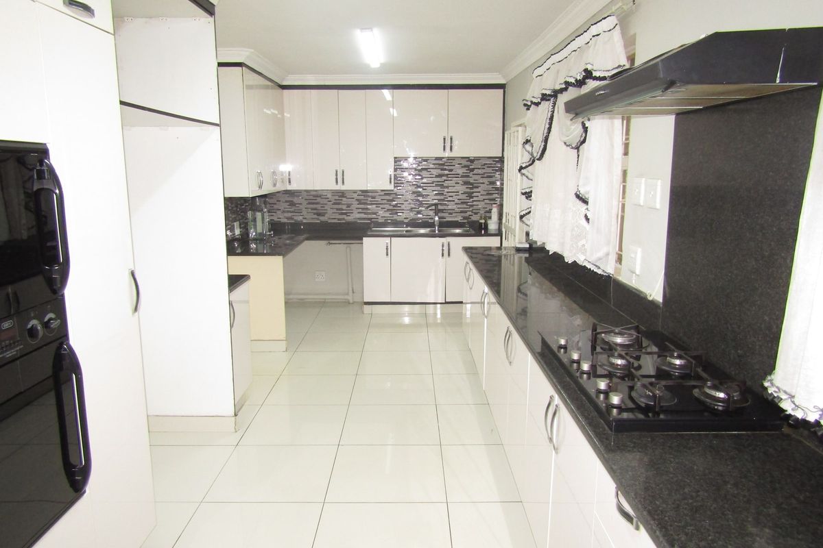 A spacious kitchen featuring white cabinetry, dark granite countertops, a gas hob with extractor fan, and tiled flooring throughout.