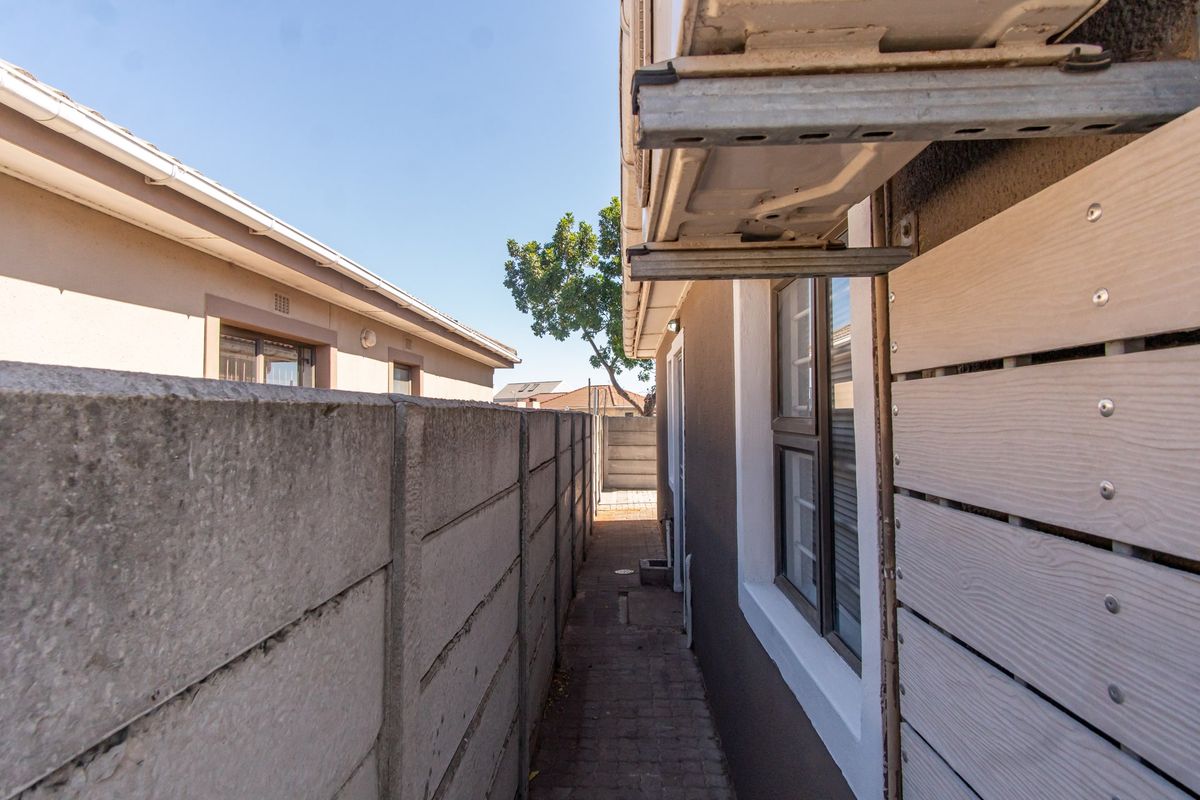 A narrow side passage featuring a concrete boundary wall, paved walkway, and exterior wall-mounted air conditioning unit.