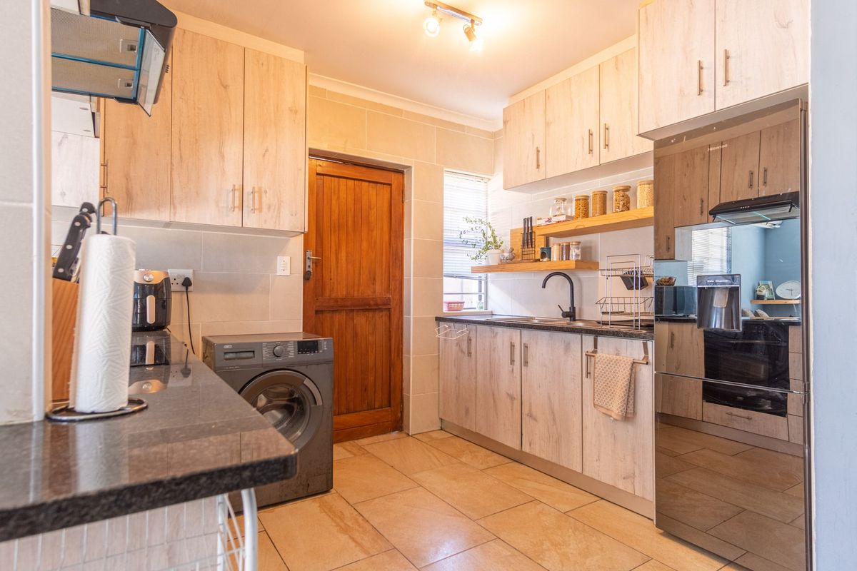 A functional kitchen featuring light wood-look cabinetry, dark granite countertops, a built-in oven, and integrated laundry space with tiled flooring.