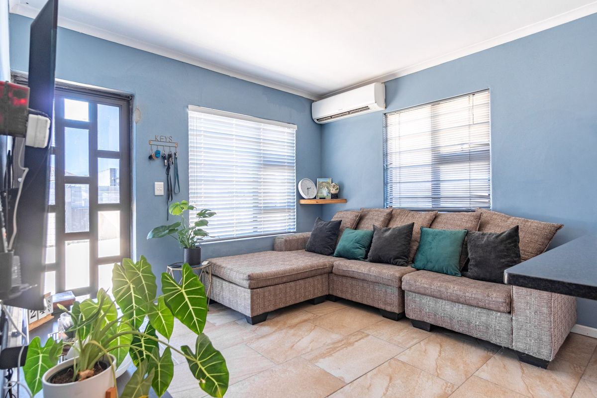 A comfortable living room featuring tiled flooring, venetian blinds, and a wall-mounted air conditioning unit.
