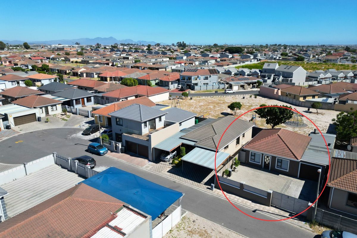 Aerial view of a residential property featuring a tiled roof, paved driveway, and perimeter walling within a suburban neighborhood.