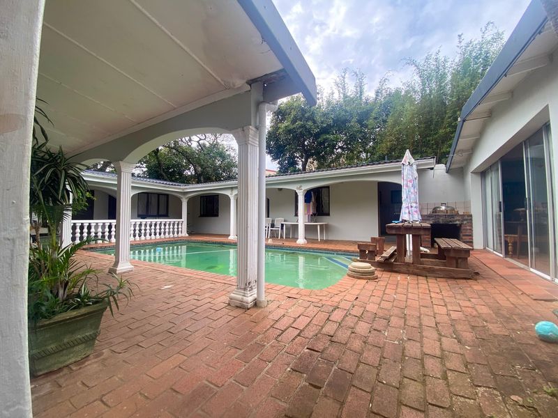 Outdoor pool area featuring a covered patio with decorative columns, brick paving, and a built-in brick braai, ideal for entertaining.