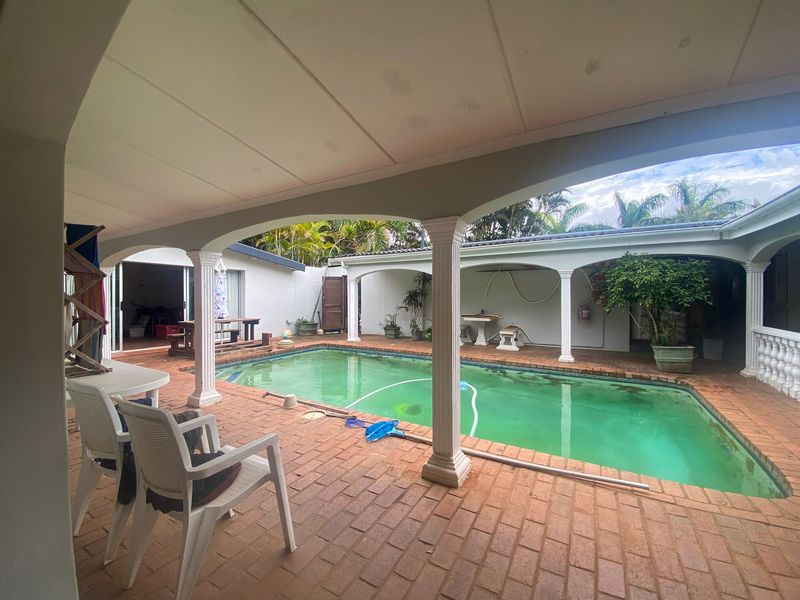 Covered patio area overlooking a swimming pool with brick paving and decorative columns, offering potential for outdoor entertainment space.