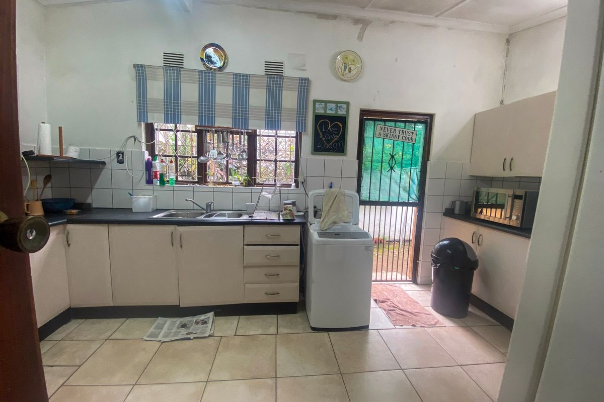 A functional kitchen featuring laminate cabinetry, double bowl sink, tiled splashback, and direct access to the exterior via a security gate.