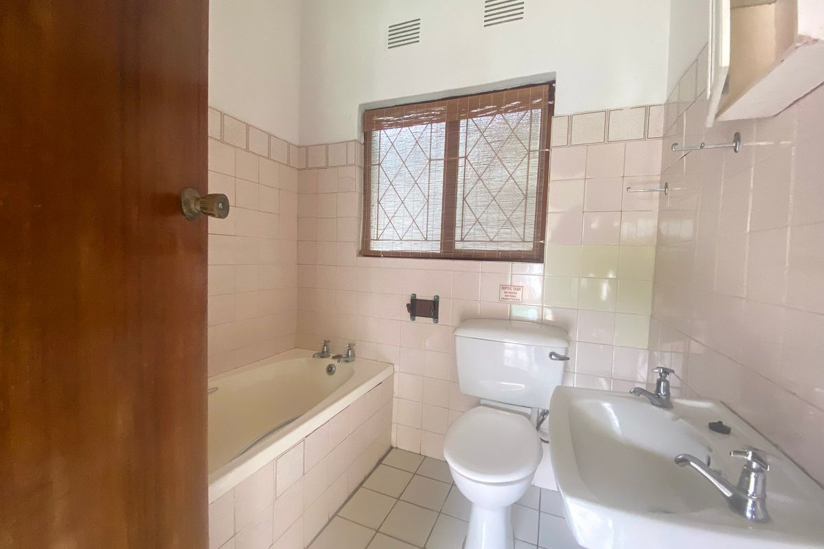 A dated bathroom featuring a built-in bathtub, pedestal washbasin, and toilet, finished with original ceramic wall and floor tiles.