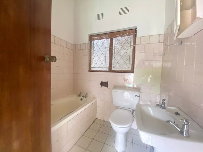 A dated bathroom featuring a built-in bathtub, pedestal washbasin, and toilet, finished with original ceramic wall and floor tiles.