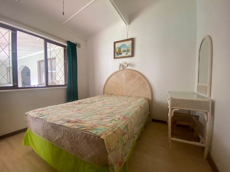 A functional bedroom featuring laminate flooring, a vaulted ceiling, and a window fitted with security bars.