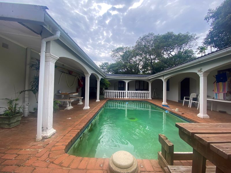 Outdoor pool area featuring a covered patio with classical columns, brick paving, and a balustrade, requiring maintenance and pool water treatment.