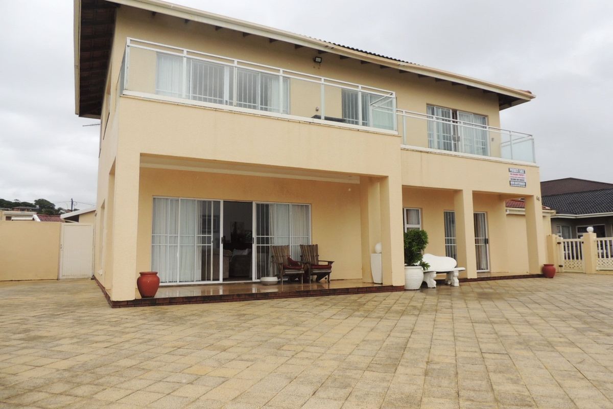 Rear view of a two-story house featuring a paved patio area, ground floor sliding doors, and an upper-level balcony with glass balustrades.