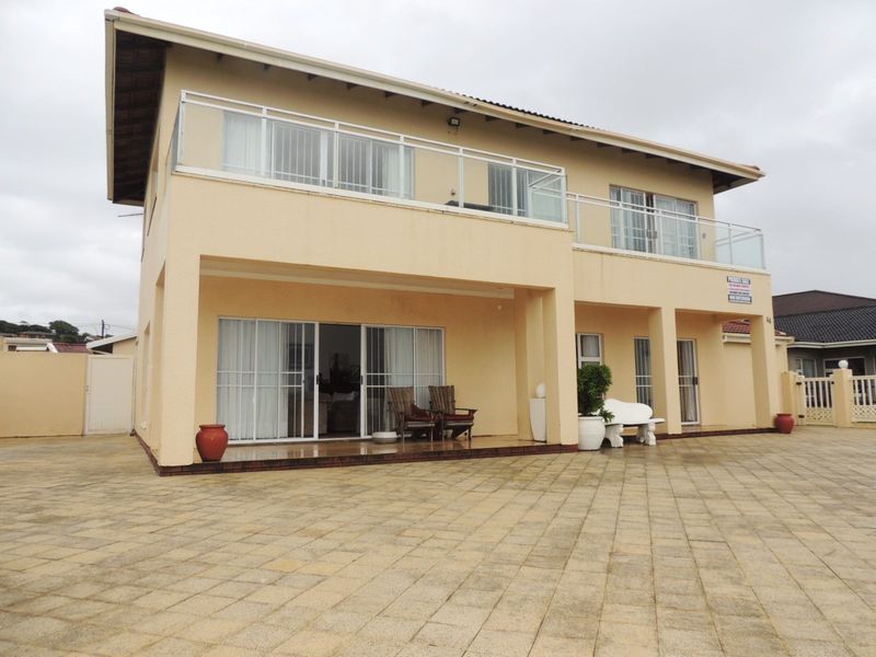 Rear view of a two-story house featuring a paved patio area, ground floor sliding doors, and an upper-level balcony with glass balustrades.